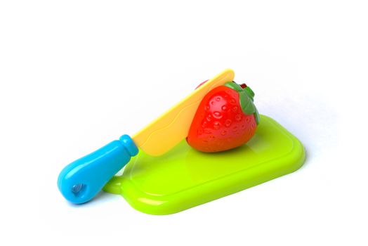A plastic toy strawberry on a cutting board being cut in half with a plastic knife.