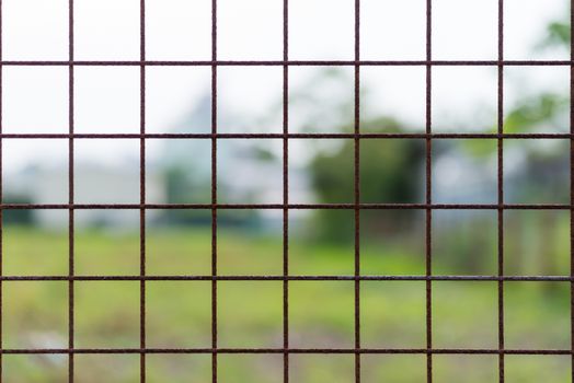 A rusty wire fence forming a pattern of squares with a blurry nature background.