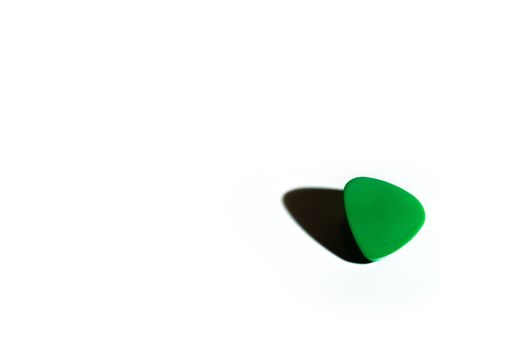 A plain green guitar pick isolated on a white background with a dramatic and dark shadow.