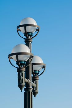 A light post with three spherical bulbs on a clear blue sky background.