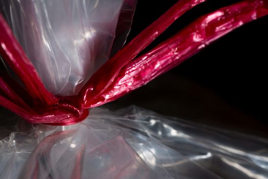 A red plastic ribbon tying closed a clear plastic bag on a black background.