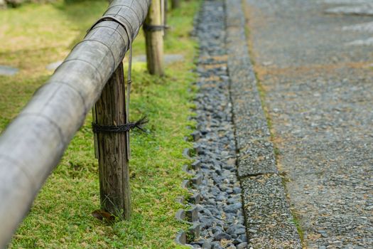A short bamboo fence along side a path lined with black stones.