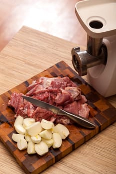 The electric meat grinder and the cut meat on a wooden chopping board