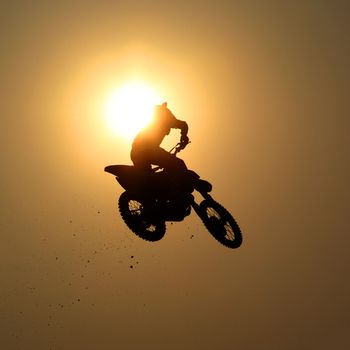 Motorcycle jumps in the air with sunset