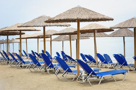 Rows of reed umbrellas and blue deck chair on the sea beach 