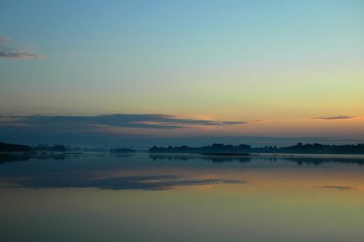 Poland.Summer dawn on the river Narew.Slight fogs and reflecting clouds in the mirror sheet of water.