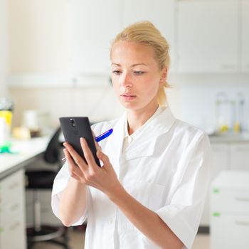 Portrait of an attractive, young, confident female health care professional in his working environment making notes on her smarth phone.