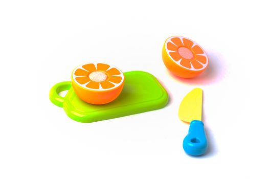 A plastic toy mikan orange on a cutting board being cut in half with a plastic knife.