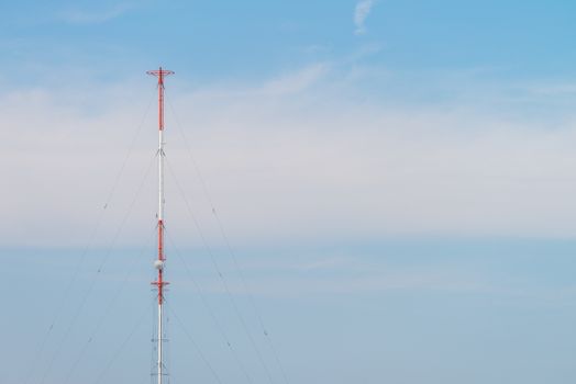 A tall red and white radio tower against a blue sky with some clouds.