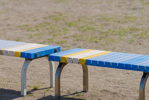 A blue, yellow and white bench on the side of a sports field.