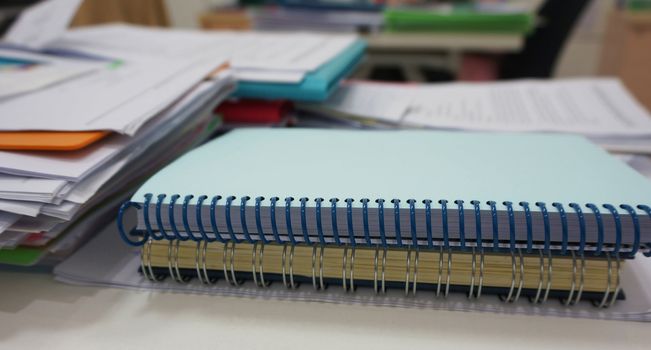 Notebook with a spiral spine and document placed on the desk in the office.                               