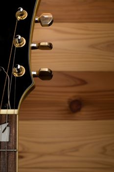 The headstock, strings, neck and tuning pegs of an acoustic guitar with a wooden wall background.