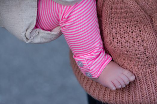 The foot and leg of a baby girl being carried by her mother, both wearing pink.