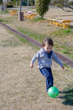 A 2 year old boy kicking a ball in a park.