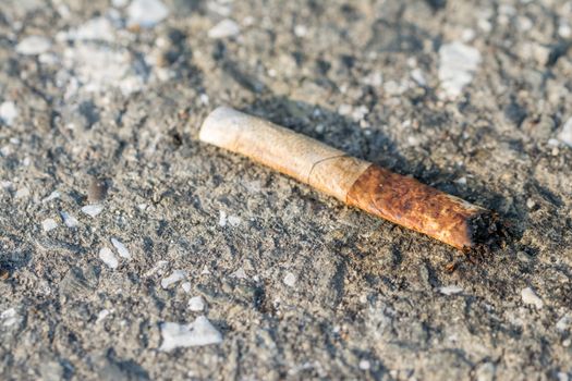 A used and dirty discarded cigarette on the ground.