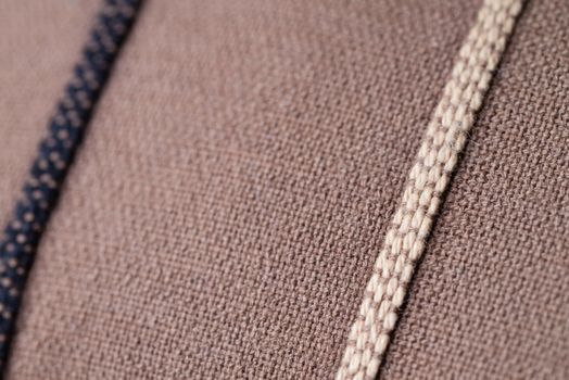 A macro shot of brown fabric on a pillow with one dark and one light brown line.