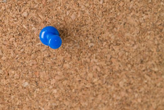 A single blue thumb tack on a cork board.