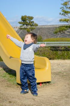 A 2 year old boy celebrating after going down a slide.