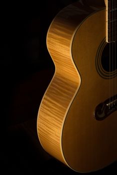 The body of an acoustic guitar lit from the side on a black background.