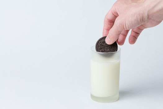 A chocolate cookie being dunked in a glass of milk.