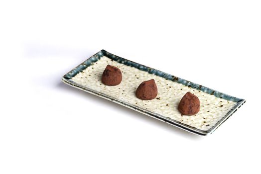Three chocolate truffles on a ceramic plate with a pure white background.
