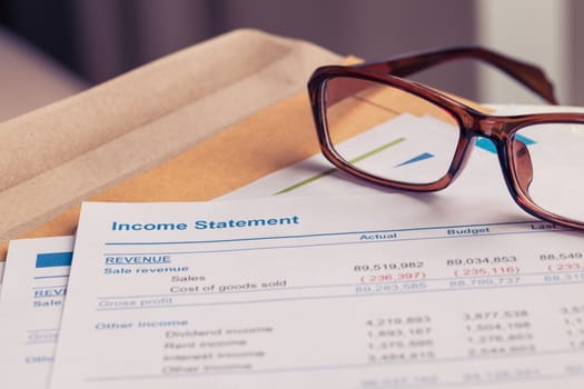 Income statement letter on brown envelope and eyeglass, business concept; document is mock-up