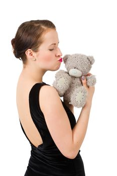 attractive smiling brunette kissing teddy bear grimacing with peg on nose in a black dress, isolated on white