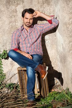 Smiling male model sitting on wooden crate with legs crossed