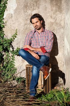 Smiling male model sitting on wooden crate with legs crossed