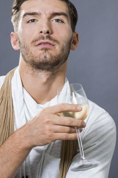 Sexy handsome young man with a beard wearing an elegant scarf drinking white wine and looking at the camera with a serious intense expression