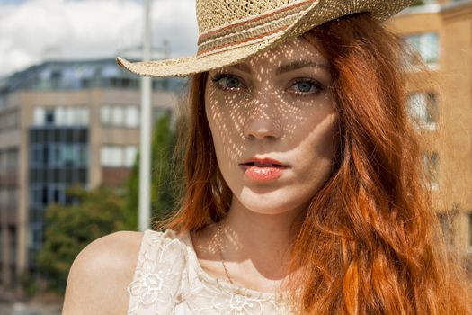 Gorgeous Woman in Hat with red hair on Cloudy Sky background