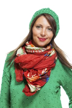 Cute sexy young woman with long brunette hair in a green winter outfit smiling playfully at the camera with her hand to her red scarf, on white