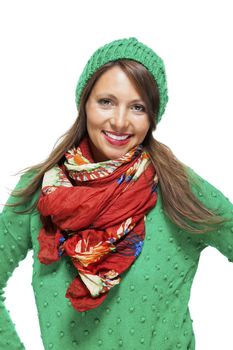 Cute sexy young woman with long brunette hair in a green winter outfit smiling playfully at the camera with her hand to her red scarf, on white