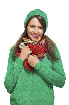 Cute sexy young woman with long brunette hair in a green winter outfit smiling playfully at the camera with her hand to her red scarf, on white