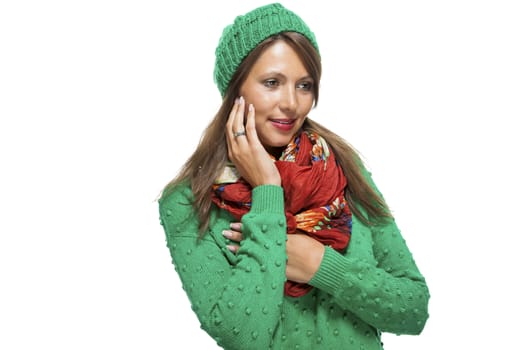 Cute sexy young woman with long brunette hair in a green winter outfit smiling playfully at the camera with her hand to her red scarf, on white