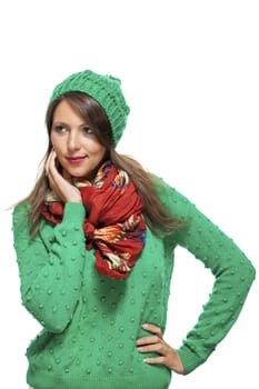 Cute sexy young woman with long brunette hair in a green winter outfit smiling playfully at the camera with her hand to her red scarf, on white