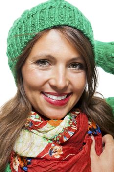 Cute sexy young woman with long brunette hair in a green winter outfit smiling playfully at the camera with her hand to her red scarf, on white