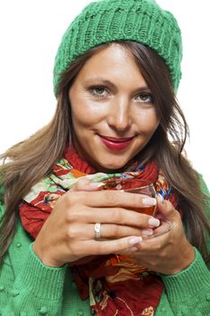 Attractive young woman in a trendy green knitted winter ensemble warming up with a cup of hot tea isolated on white