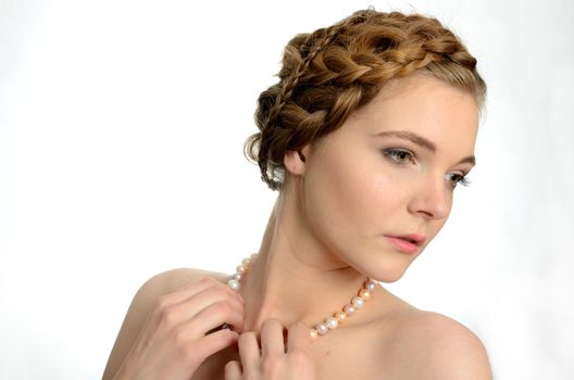 Portrait of young girl, kind face expression. Girl wears pearls and holds them by hands.