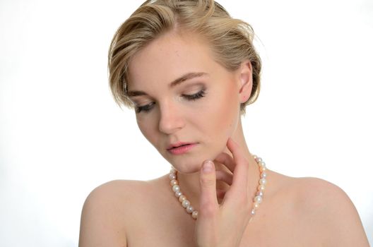 Model with soft face expression. Kind girl wears pearl on her neck, one hand near face.