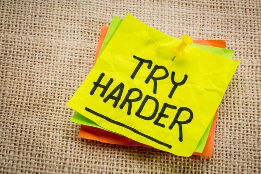 try harder - motivation words on a  yellow sticky note against burlap canvas