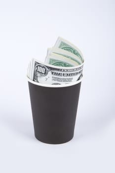 Close up front view of black paper glass with banknotes of one hundred dollar inside, isolated on white background.