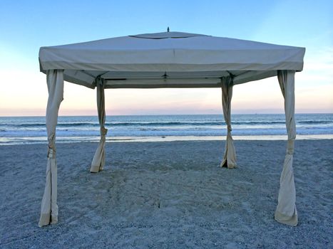 A cabana with it's sides tide back on the beach at sunset