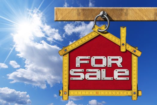 
Yellow wooden meter ruler in the shape of house with text for sale. For sale real estate sign on blue sky with cloud and sun rays