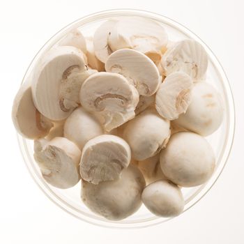 Button mushrooms, whole and sliced, in glass bowl and isolated on a white background.  View from directly above.