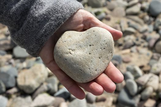 A heart shaped stone in a hand on a beach