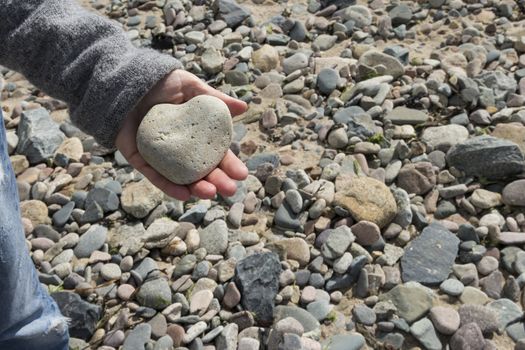 A heart shaped stone in a hand on a beach with some pebbles