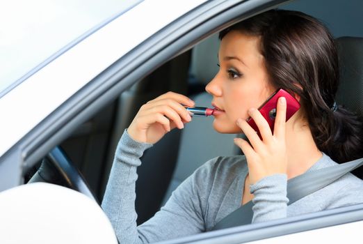 Female driver talking by mobile telephone and doing make-up.