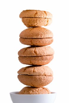 Neatly stacked tower of freshly baked macaroons balancing in a bowl centered over a white background, side lit