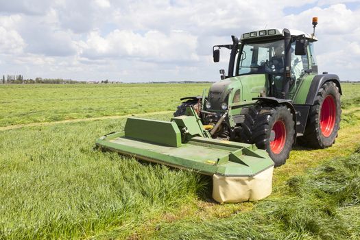 tractor and mower in green meadow in the netherlands on sunny day